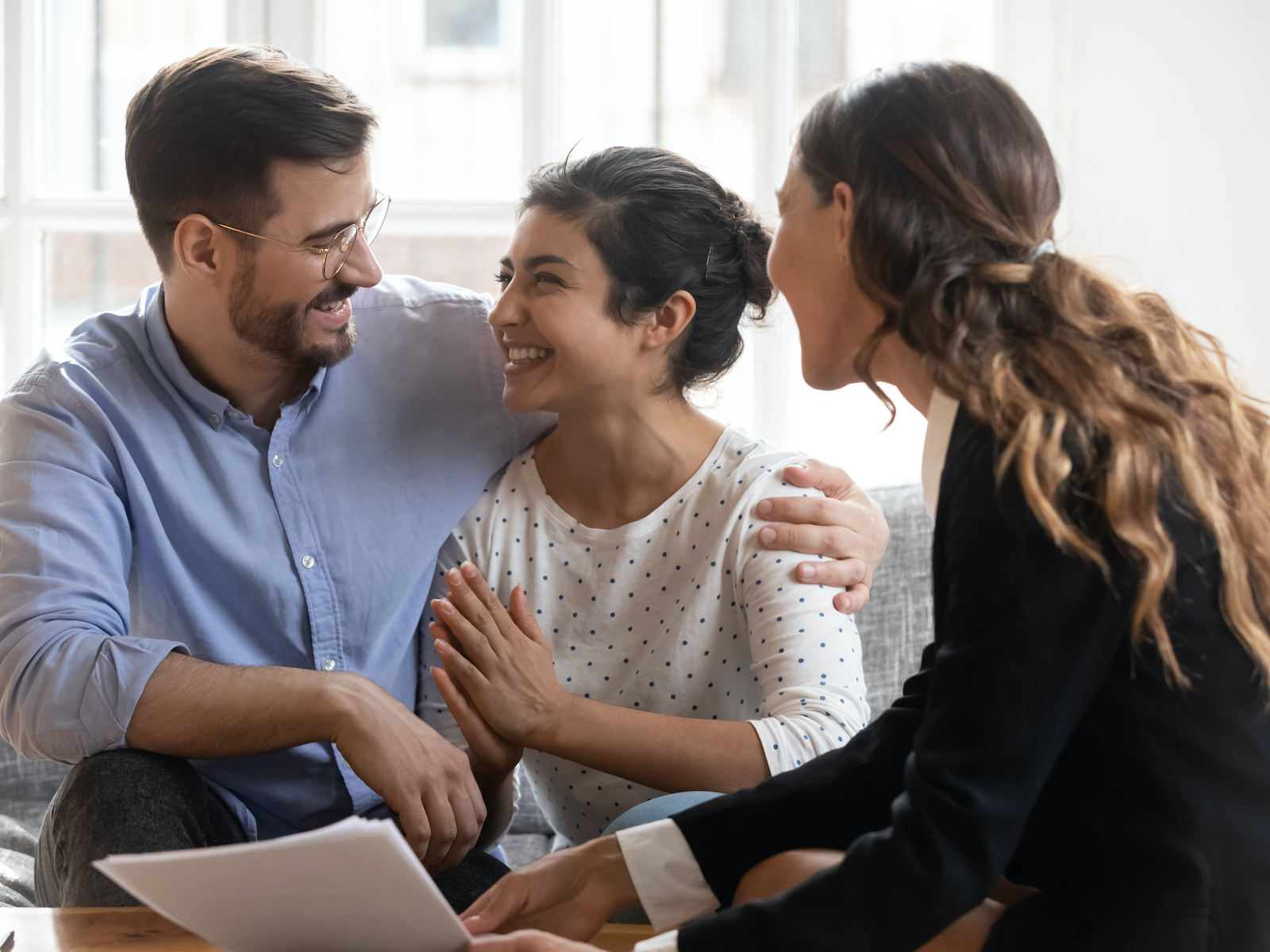 Search Now Happy diverse couple making decision at meeting with advisor, looking at each other, smiling Indian woman and Caucasian man purchasing new apartment, taking loan or mortgage, satisfied clients
